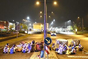 Straßenblockade, Aktivisten sitzen auf der Fahrbahn, rings herum ist es dunkel und es brennen Laternen.