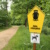 Bäume, Sträucher und gelbes Naturschutz-Schild.