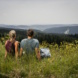 Rückenansicht von Mann und Frau, beide sitzen auf einer Bergwiese und blicken in die Ferne.